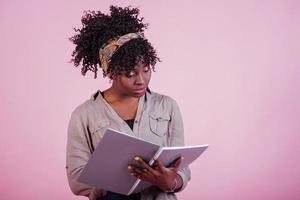 Preparing for exam. Attractive afro american woman in casual clothes at pink background in the studio photo