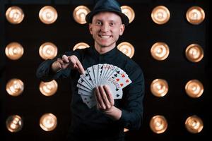 He's takes your card. Magician in black suit standing in the room with special lighting at backstage photo