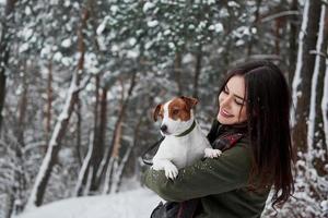 Hugging the pet and enjoying the moment. Smiling brunette having fun while walking with her dog in the winter park photo