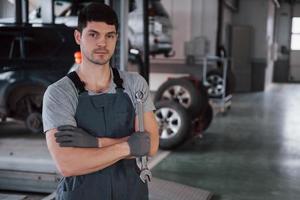 Waiting for customer. Portrait of serious worker in uniform that stands in his workshop with wrench in hand photo