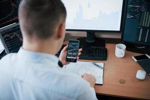Financial report on the one big graph n the smartphone. Man working online in the office with multiple computer screens in index charts photo
