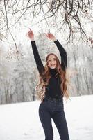 calentamiento por los movimientos. linda chica con cabello largo y blusa negra bailando en el bosque de invierno foto