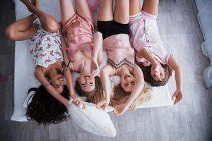 Daylight in the room. Inverted portrait of charming girls that lying on bed in nightwear. Top view photo