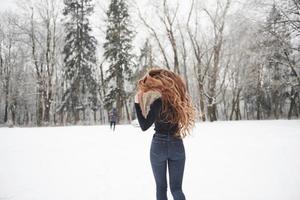 Man is in front of woman. Rear view of girl with long hair runs near the forest to the automobile in wintertime photo
