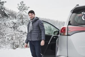 buscando a donde ir. un tipo con una bufanda larga en el cuello sale del camión para dar un paseo por el bosque nevado de invierno foto