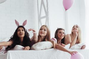 Balloons up into the air. Joyful girls in the nightwear lying on the bed in white room and have celebration photo