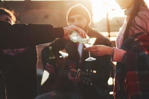 Pouring alcohol. Friends have fun at rooftop party with decorative colored light bulbs photo