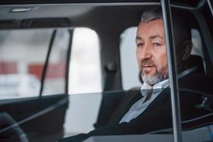 Break between trip. Senior businessman in official clothes sitting in a modern new car photo