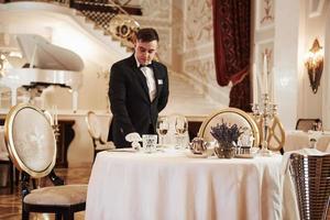 Everything must be perfect. Process of preparing place for special visitors. Waiter in classical wear works on the servering photo