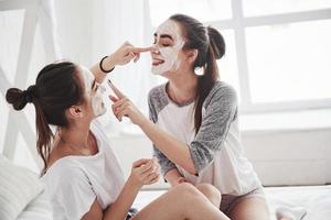 What to do when waiting for the results. Conception of skin care by using white mask on the face. Two female sisters have weekend at bedroom photo