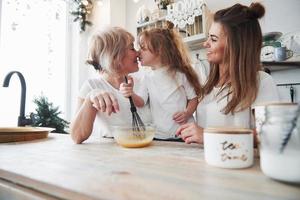 Give me kiss. Mother, grandmother and daughter having good time in the kitchen photo