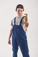 Plumber is ready to help. Man in blue uniform stands against white background in the studio photo