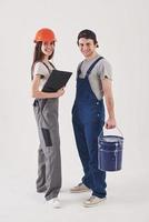 Working together. Man in blue uniform with woman in hard hat stands against white background in the studio photo