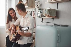 dulce serenata. joven guitarrista tocando una canción de amor para su novia en la cocina foto