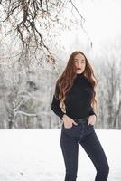 Pretty girl with long hair and in black blouse is in the winter forest photo