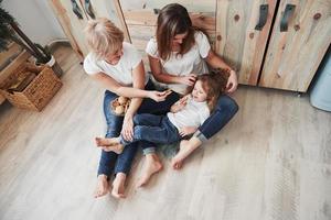 Kid lying on the parent's legs. Mother, grandmother and daughter having good time in the kitchen photo