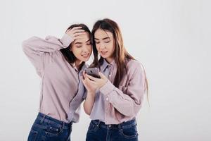 Modern technology. Two sisters twins standing and posing in the studio with white background photo