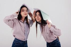 Just having fun with notepads holding on heads. Two sisters twins standing and posing in the studio with white background photo