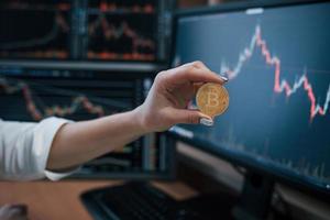 Exchange conception. Woman's hand holding bitcoin in modern office with many monitors with graphs photo