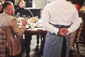 From the back of waiter. Family friends having nice time in beautiful luxury modern restaurant photo