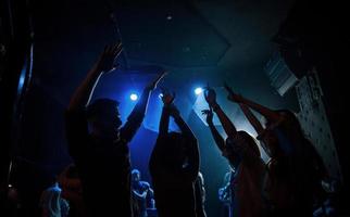 con los brazos levantados. grupo de personas que disfrutan bailando en la discoteca con hermosas luces foto