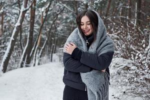 Warming with some good clothes. Portrait of charming woman in the black jacket and grey scarf in the winter forest photo