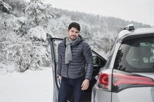 Guy with long scarf on the neck is walking out from the car to have a walk in winter snowy forest photo