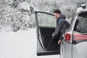 Looking into the camera. Guy with long scarf on the neck is walking out from the car to have a walk in winter snowy forest photo