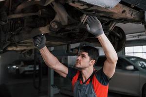 Owner will be satisfied. Man at the workshop in uniform fixes broken parts of the modern car photo