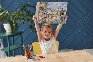 Proudly raised up her creation. Cute little girl in art school shows her first paintings drawn by pencils and markers photo