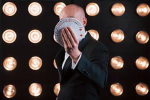 Focused photo on playing cards. Magician in black suit standing in the room with special lighting at backstage