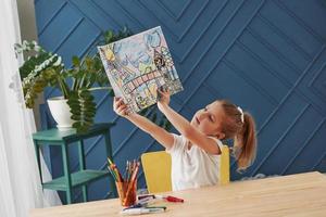 Admiring her creation. Cute little girl in art school shows her first paintings drawn by pencils and markers photo