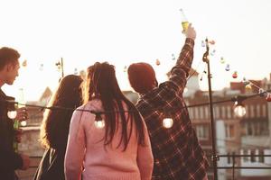 saludar a los vecinos. vacaciones en la azotea. alegre grupo de amigos levantaron la mano con alcohol foto