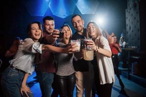 bailemos toda la noche. grupo de jóvenes amigos sonriendo y haciendo un brindis en el club foto