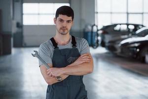 All for your vehicle. Portrait of serious worker in uniform that stands in his workshop with wrench in hand photo