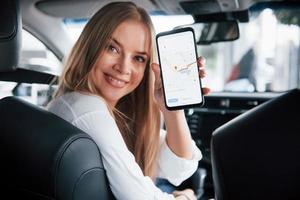 Route is done. Beautiful blonde girl sitting in the new car with modern black interior photo