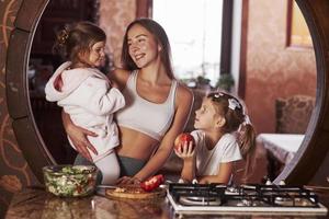 miembros de la familia felices. madre joven con niños de pie en la cocina y divertirse foto