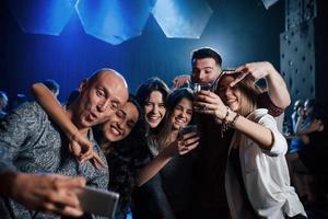 haciendo cara graciosa. amigos tomando selfie en una hermosa discoteca. con bebidas en las manos foto