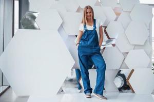 Reflection of wheel. Girl in blue uniform stands against abstract wall with white pieces of surface in the shape of hexagon in the auto saloon photo