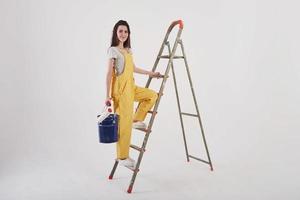 Spacious room. Beautiful brunette in yellow uniform and blue colored bucket stands near the ladder photo