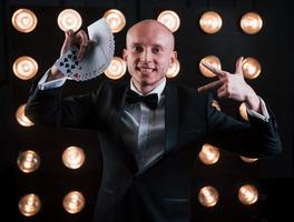 Showing some gestures. Magician in black suit and with playing cards standing in the room with special lighting at backstage photo