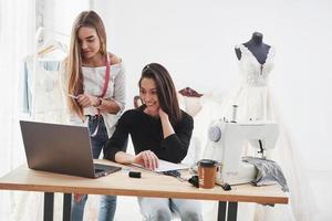 Looking on the laptop. Two female fashion designers works on the new clothes in the workshop photo