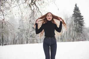 en el claro. linda chica con cabello largo y blusa negra está en el bosque de invierno foto