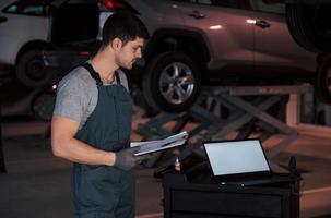 Graphs on the paper. Worker stands indoors in uniform does reports, calculations and looking at the plans photo