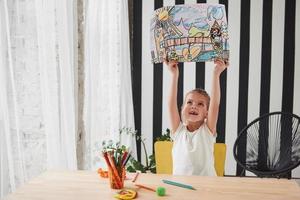 Isn't it beautiful piece of art. Cute little girl in art school shows her first paintings drawn by pencils and markers photo