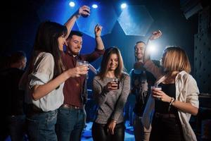 Girl is in the center of attention. Happy people dancing in the luxury night club together with different drinks in their hands photo