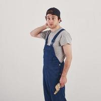 Touching the hat. Man in blue uniform stands against white background in the studio photo