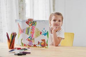 Nice daylight. Cute little girl in art school shows her first paintings drawn by pencils and markers photo