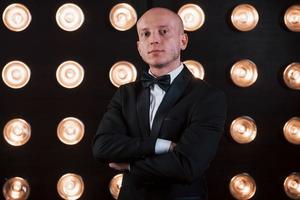 Nice portrait of professional illusionist. Magician in black suit standing in the room with special lighting at backstage photo