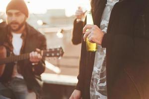 Bottle with beer. Rooftop party with some alcohol drinking and guitar playing. Sunshine behind photo